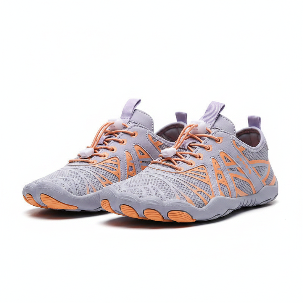 A person wearing light purple athletic sneakers with orange geometric accents, standing on a sandy beach with the ocean blurred in the background.