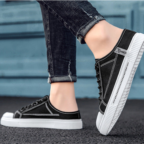A person wearing black low-top canvas sneakers with white soles, shown from the knees down against a blue-gray outdoor wall. The top of the image has a black banner with white text reading 'MODEL LOCATION DISPLAY'.