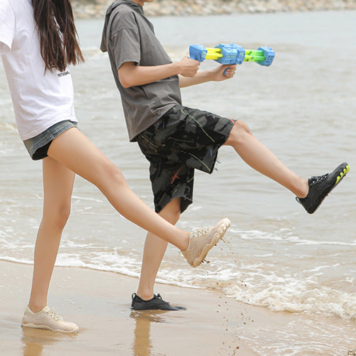 Two people walking on a beach near the shoreline, one holding a blue and green water toy. The photo is centered within a blue border.