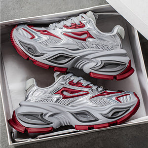 A pair of chunky platform sneakers in white, gray, and red, displayed inside an open white shoebox on a gray surface.