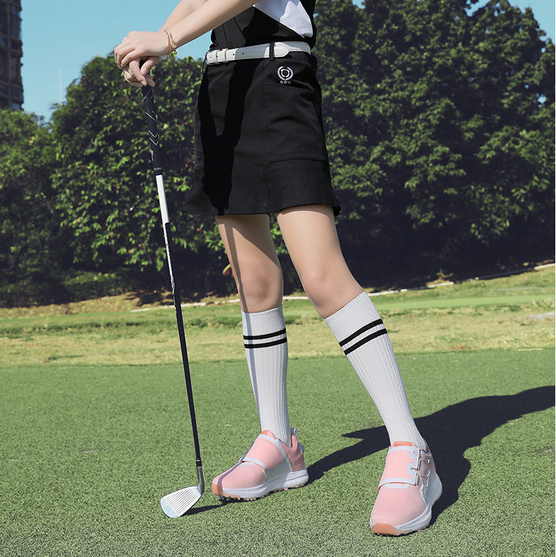 A woman on a golf course wearing a black and white short-sleeve golf dress, a black skirt, white knee-high socks, and pink golf shoes, holding a golf club.