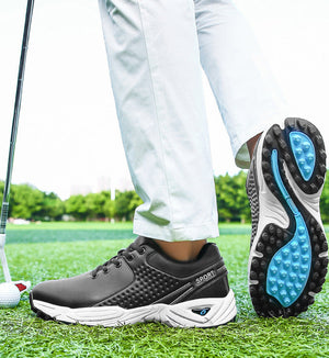 A pair of black and white golf shoes with bright blue accents, shown on a golf course. One shoe is worn with white pants, and the other is turned around to show its textured black and blue sole.
