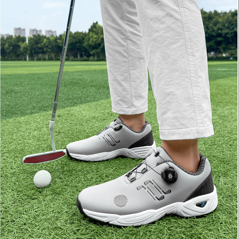 A person wearing light gray and white golf shoes with a dial closure system, standing on a green golf course next to a golf club and a golf ball.