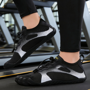 Black and silver minimalist toe-loop athletic shoes worn on a person's feet in a gym setting.