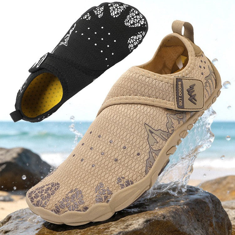 A pair of slip-on water shoes shown on a beach background, with one shoe floating above the water and one resting on wet rocks. The top shoe is black with white speckled patterns and a yellow interior, while the bottom shoe is beige with a textured knit upper and a small brown brand tab.
