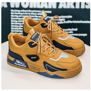 A pair of low-top sneakers in mustard yellow, navy blue, and light gray, displayed on a white surface with a dark graphic background.