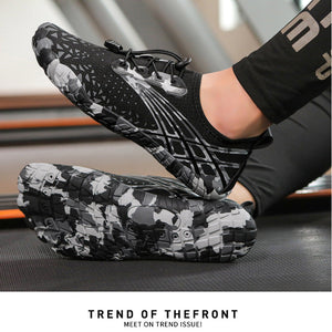 A person wearing black athletic sneakers with a gray and white abstract geometric pattern, shown on a treadmill. The shoes feature a knit upper, black laces, and a textured sole.
