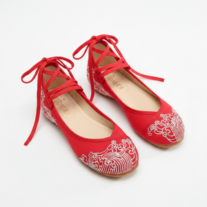 A pair of red flat shoes with white wave embroidery on the toe and side, featuring lace-up front straps and a low heel, photographed on a clean white background.
