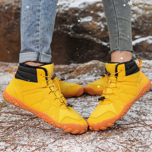 A person wearing bright yellow mid-calf waterproof boots with black ankle collars, standing outdoors on a snowy rock surface. The image includes text overlays reading 'Thickened plush' and 'Comfortable mid-top with cold-resistant warmth'.