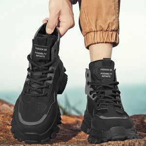A person outdoors wearing a pair of black mid-calf lace-up boots with chunky soles, standing on a rock with a blurred ocean background. One hand is lifting the left boot to show the interior and tongue label that reads 'FASHION 5K POSSIBILITY INFINITE'.