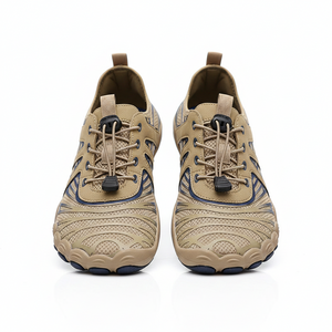 A pair of beige and brown athletic water shoes with dark blue accents, shown being worn on a sandy beach with the ocean in the background.
