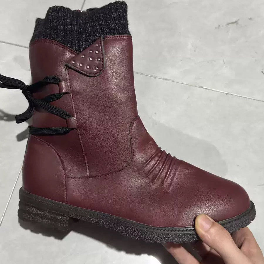 A dark burgundy leather ankle boot with a black knit sock-style collar, black laces, and a black sole, held by a hand against a light gray tiled floor.