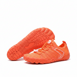 A pair of bright orange mesh athletic water shoes with white laces and white trim, displayed on a light wooden surface with a blue gradient background and a wire stand.