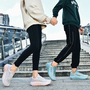 Two people walking hand in hand up outdoor stone stairs, wearing athletic tracksuits and sneakers. The left person wears a light beige oversized sweatshirt and black leggings with white sneakers.
