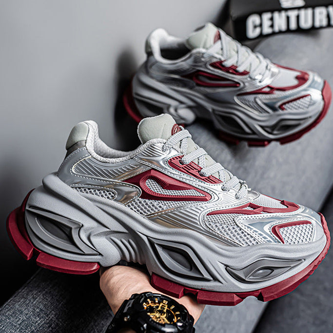 A pair of chunky low-top sneakers in white and gray with red accents, shown with one shoe being held by a hand. The background is a gray textured surface with a black and white 'CENTURY' sign.
