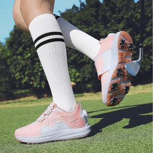 A person wearing pink and white golf shoes with white knee-high socks featuring black stripes, standing on a green golf course with trees in the background.