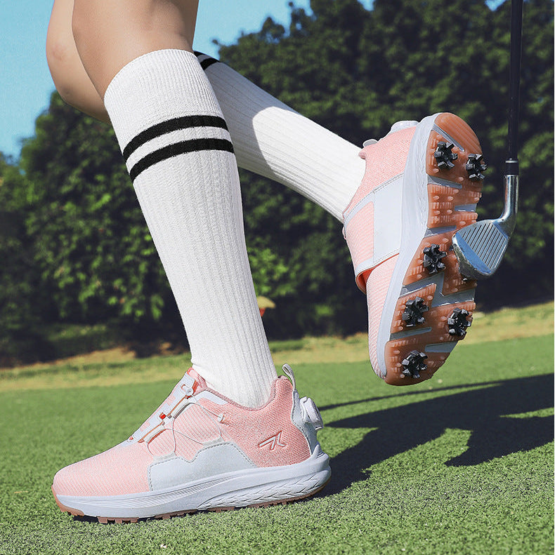 A person wearing pink and white golf shoes with white knee-high socks featuring black stripes, standing on a green golf course with trees in the background.