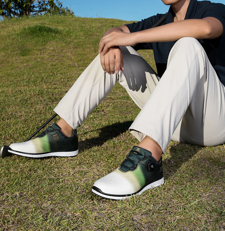 A person sitting on grass outdoors wearing a pair of low-top athletic shoes with a white and dark green gradient design, black soles, and hook-and-loop strap closures.