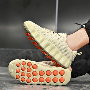 A close-up of a person wearing a light beige knit sneaker, with the sole showing bright orange circular cushioning details, set against a dark gray background.