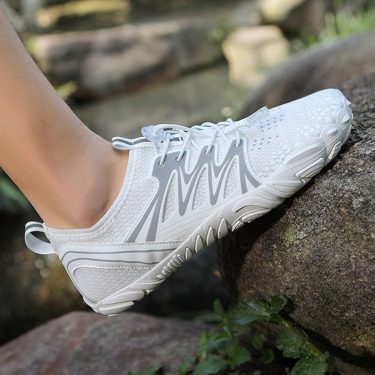 A white athletic shoe with gray wavy side stripes, shown worn on a person's foot resting on a large rock outdoors.