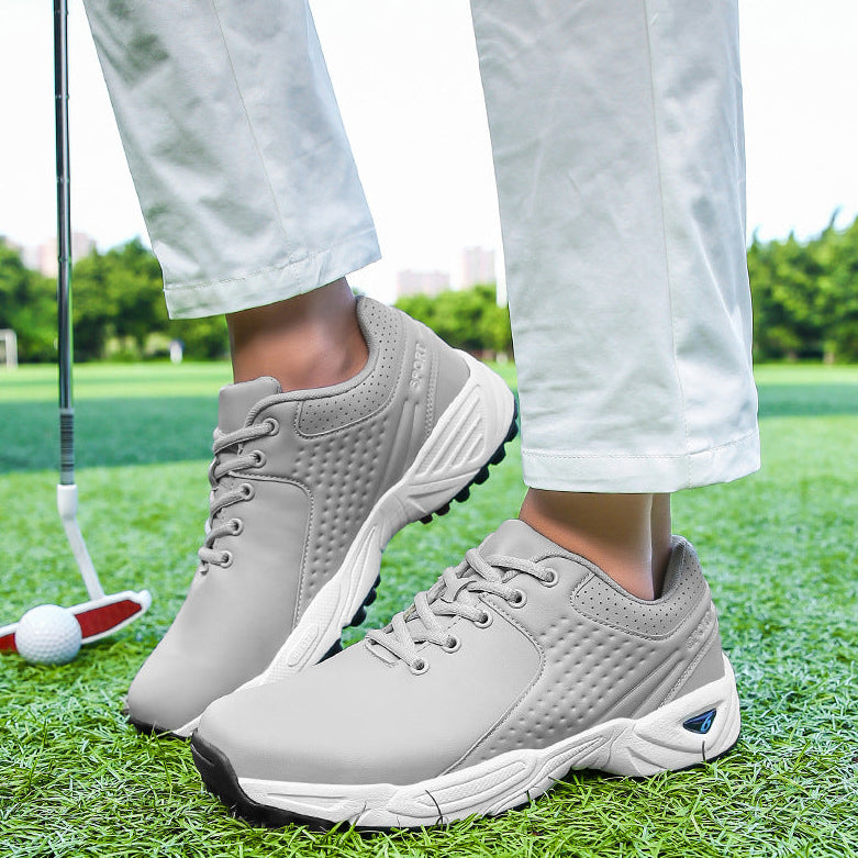 A person wearing light gray golf shoes on a green golf course, with white pants visible from the knees down and a golf club in the background.