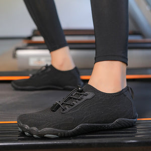 Black minimalist slip-on sneakers worn on a person's feet while standing on a treadmill in a gym.