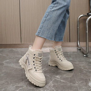 A person wearing beige lace-up ankle boots with chunky soles and light blue cropped jeans, standing on a gray marble floor in front of a wood-paneled wall.