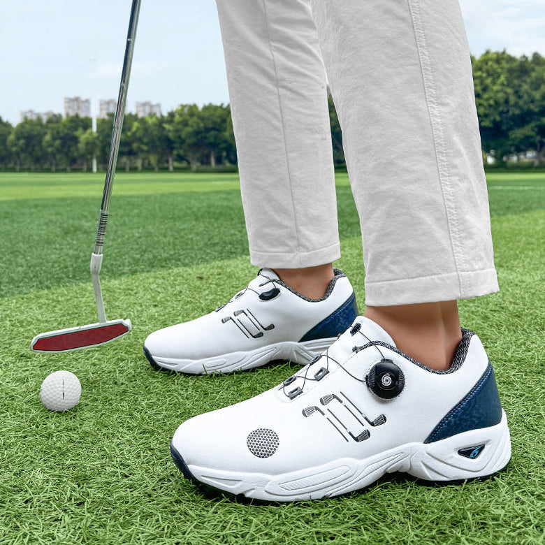 White and navy blue golf shoes with a dial closure system, shown on a person standing on a green golf course next to a golf putter and ball.