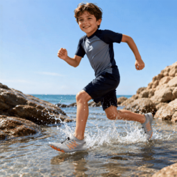 Child wearing gray and orange Tidepool Junior quick-dry water shoes near the water